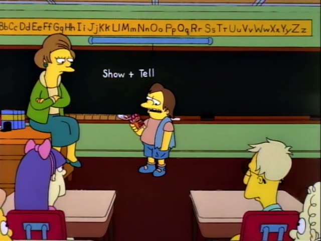 Nelson stands at the front of a classroom holding up a ketchup bottle while his teacher, Mrs. Krabappel with her tall brown…