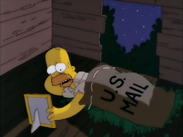 Homer sits in a dim wooden room at night, holding a gold-framed picture and staring at it while a U.S. MAIL sack lies…