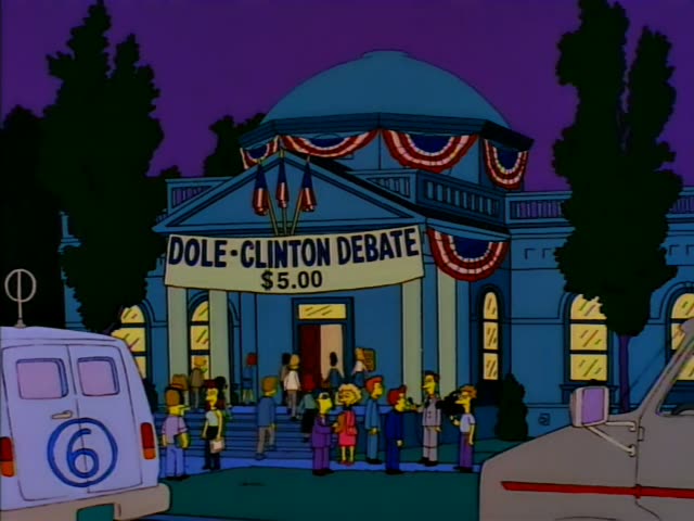 Lisa stands near the front of a crowd of Springfield residents waiting on the steps of a domed blue hall beneath a banner…