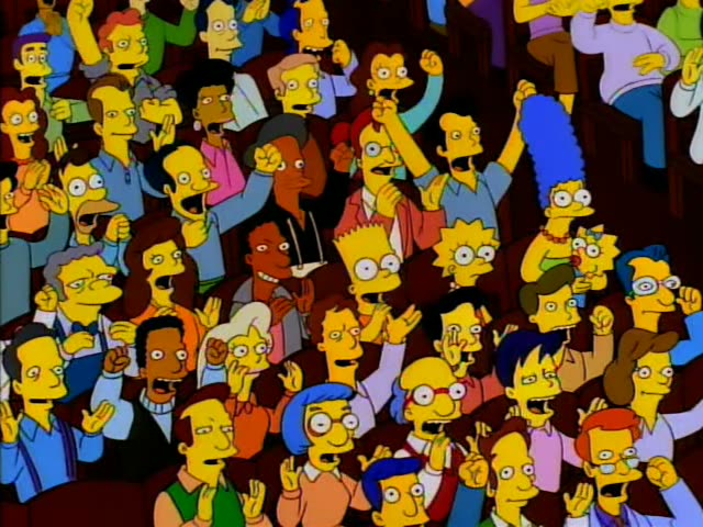 Bart, Lisa, Marge and baby Maggie sit among a cheering, hand-waving crowd in a packed hall with a red curtain