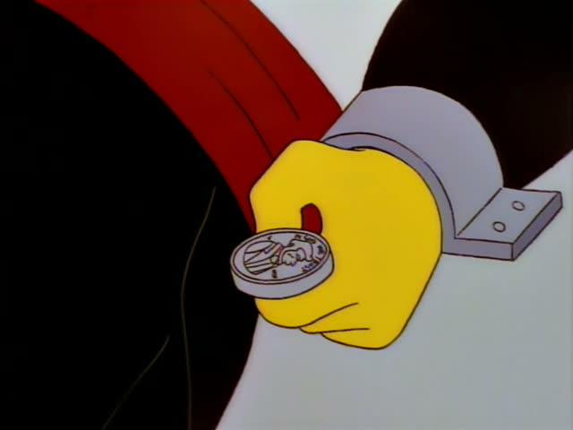 A dark-haired man in a black suit fires a red laser beam from a pen at a table with sparking, shoe-shaped objects on it…