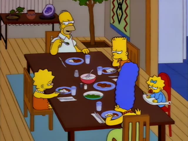 Homer, Marge, Bart, Lisa and baby Maggie sit around a wooden dining table in a bright room with a potted tree and a wall…