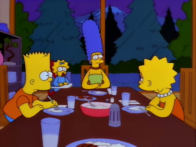 Bart, Lisa, Maggie and Marge sit around a dark wooden dining table in a lakeside cabin with a window showing pine trees…