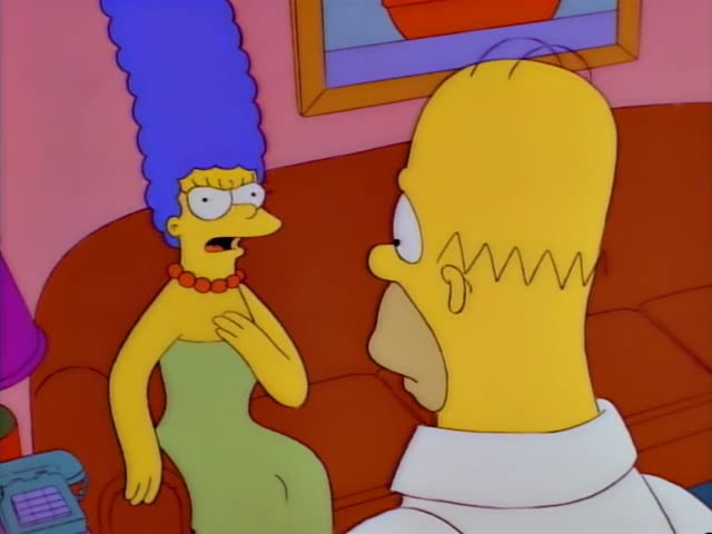 Marge sits on a red couch in the living room and talks to Homer, the bald man in a white shirt seen from behind