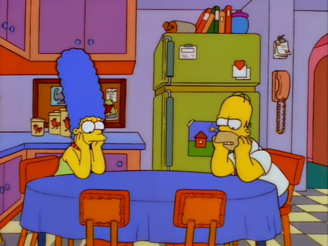 Marge Simpson and Homer Simpson sit at a blue-draped kitchen table in their cartoon home