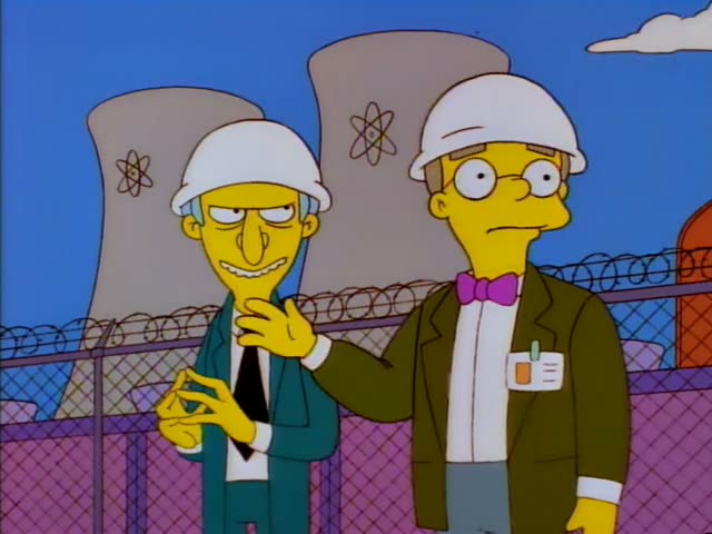 Mr. Burns and his thin assistant Smithers in a white hard hat and glasses stand before cooling towers and a barbed-wire…