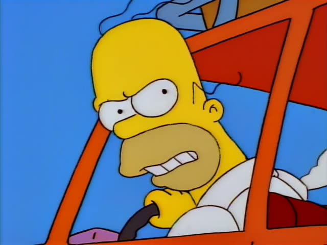 Homer Simpson grips the steering wheel of an orange station wagon, grimacing and glaring sideways with his mouth open…