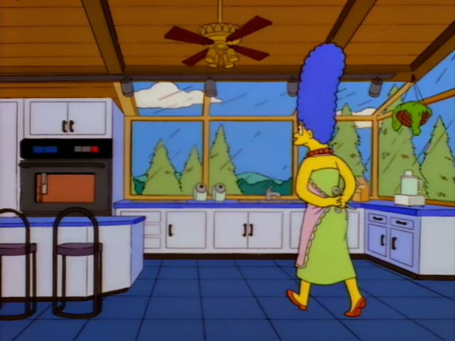Marge Simpson is in a wood-ceilinged kitchen with a wall oven glowing orange, bar stools, and a window showing pine trees