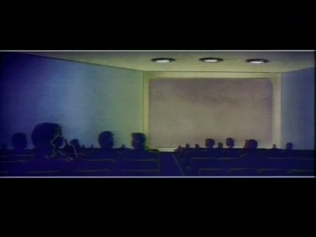 A row of dark silhouetted audience members, one on the left with a tall bouffant hairdo, sits in a theater facing a blank…