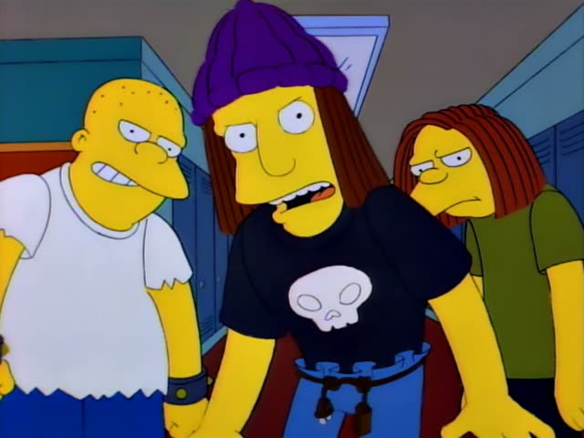 Three unfamiliar teenagers stand in a school hallway lined with lockers: a bald, heavyset boy in a white shirt…