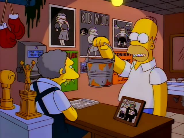 Homer stands at a bar counter holding up a metal spit bucket with one hand, then lifts a framed photo while Moe leans…