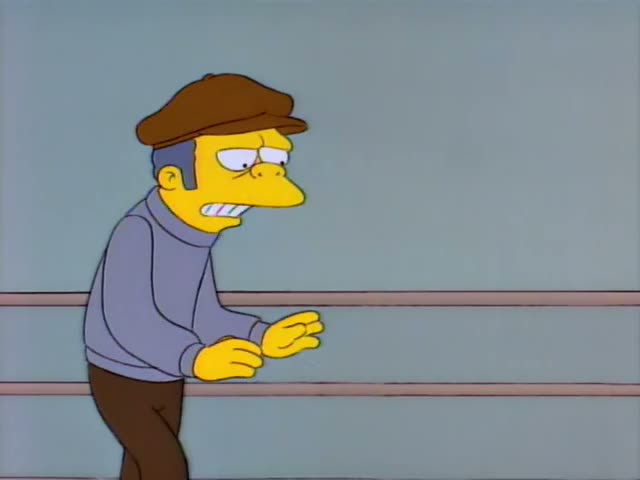 Homer Simpson leans against the ropes of a boxing ring while a slim older man in a brown flat cap and grey turtleneck…
