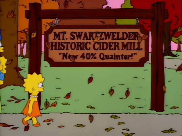 Lisa stands beside a wooden sign reading "Mt. Swartzwelder Historic Cider Mill, Now 40% Quainter!" as autumn leaves drift…