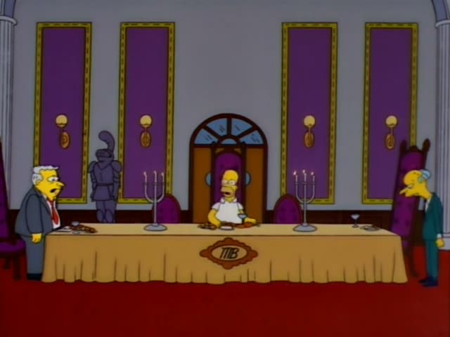 Homer sits alone at a long gold-draped table marked with a TMB emblem, while Mr. Burns stands at the right end…