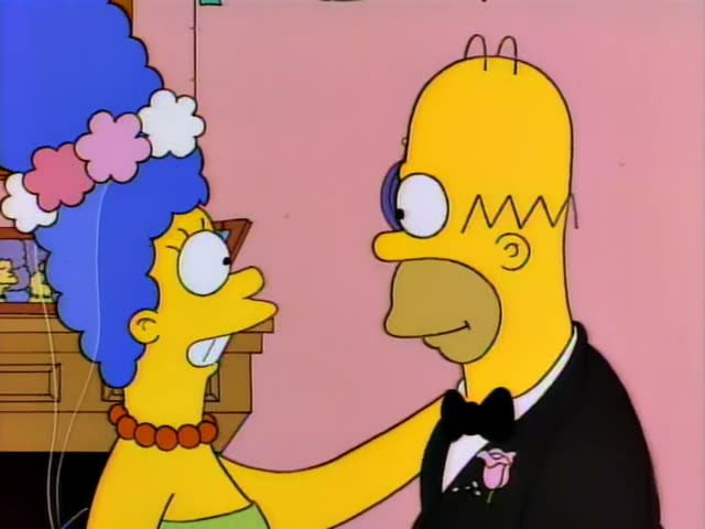 Marge and Homer stand close together in a pink room with a wooden cabinet, framed family portraits and a small wall sconce