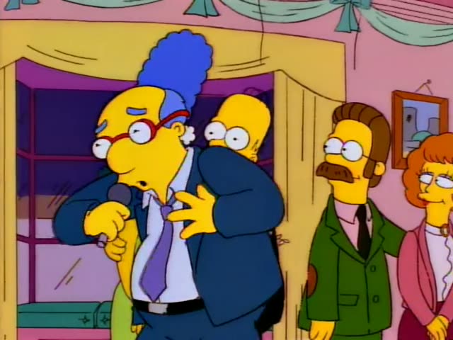 Marge stands beside a heavy bald man with red-rimmed glasses and a blue fringe of hair, dressed in a dark suit and purple…