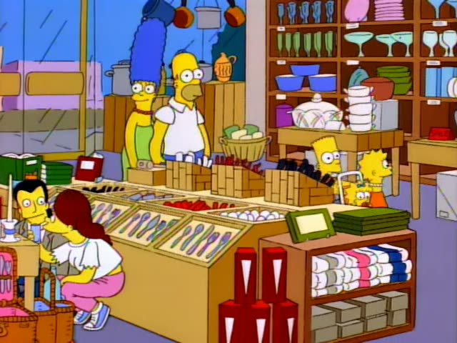 Marge Simpson stands at a kitchenware store counter while Homer stands behind her, and Bart, Lisa, and Maggie…