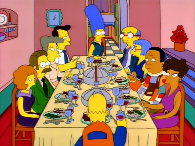 Bart sits at the front of a long dining table with Ned Flanders in his green sweater and moustache on the left, Marge…