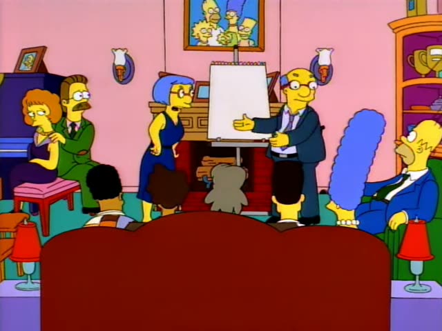 In a pink living room with a fireplace, Ned Flanders in a green sweater sits beside a red-haired woman, while Marge…