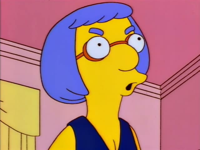 Marge Simpson with her tall blue beehive and Homer sit on a red couch in a pink living room, with Lisa standing nearby