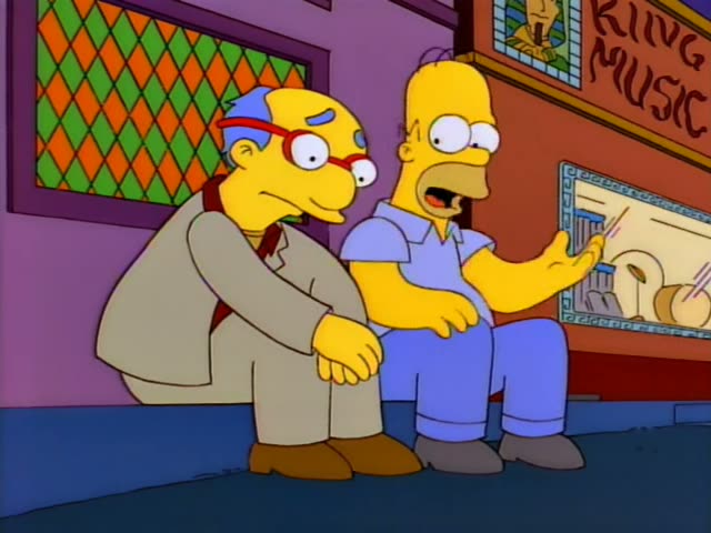 Homer sits on a bench beside a balding man in red-framed glasses and a tan suit, both in front of a shop with a 'KING MUSIC'…