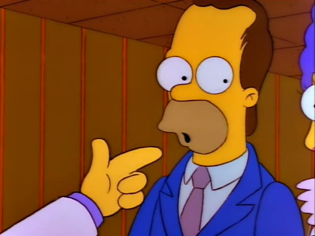 Homer and Marge stand at a wedding chapel while a thin-moustached man in a white suit and red tie, with slicked-back black…