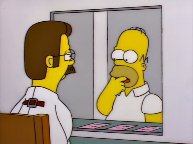 Homer and Ned Flanders sit facing each other across a small room with a microphone and pink cards on a table