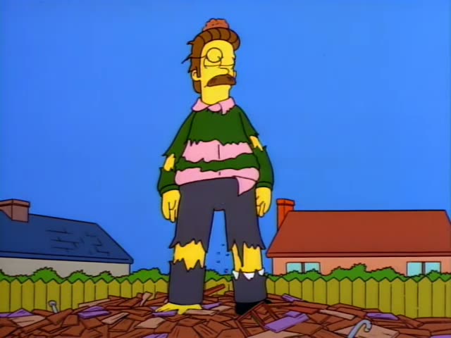 Ned Flanders stands atop a heap of splintered wooden planks in his fenced backyard, with a neighborhood of houses and hills…