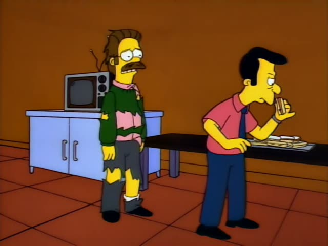 Ned Flanders stands in a room with white cabinets, a microwave and a tray of food on a dark table, while a dark-haired man…