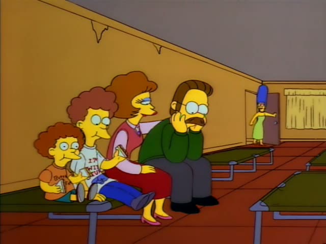 Ned Flanders sits on a green cot with his hand on his chin, beside a woman with reddish curly hair in a pink sweater and red…