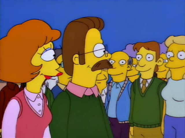 Ned Flanders in a green sweater and Homer Simpson in an orange cap, white shirt and tool belt stand before a crowd…