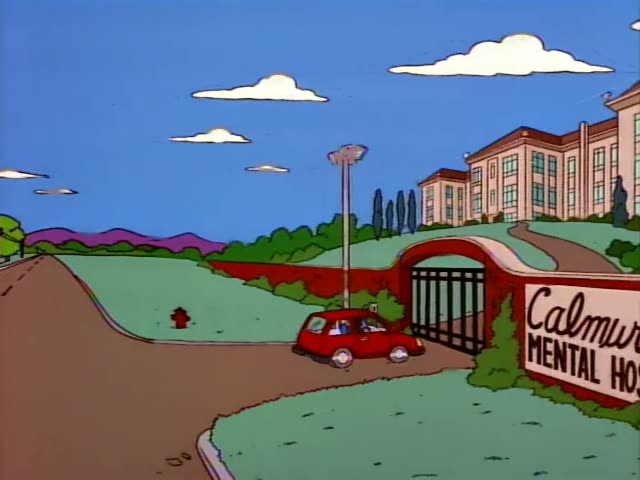 A small red car, its driver barely visible and not identifiable, drives along a winding road toward the entrance of Calmwood…