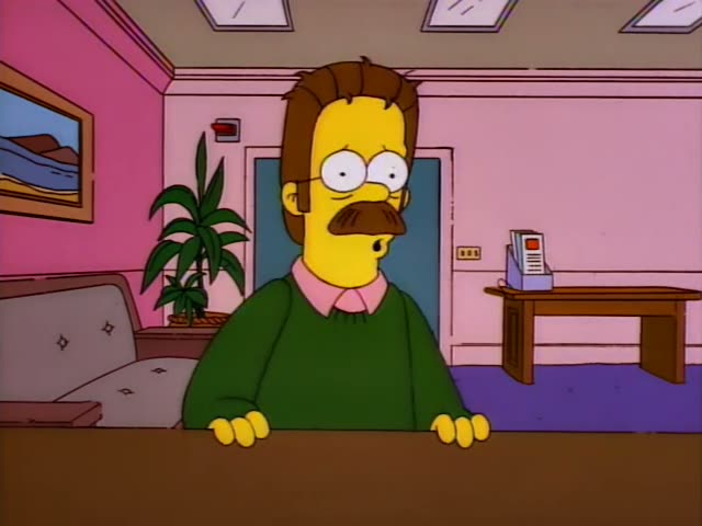 Ned Flanders stands behind a counter in a pink office with a potted plant, a sofa and a desk holding a small box of papers