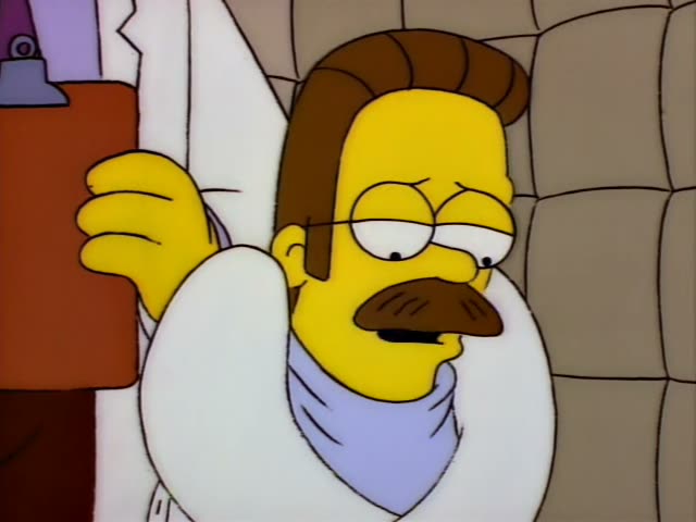Ned Flanders sits in a white straitjacket against a padded grey wall in a sanitarium