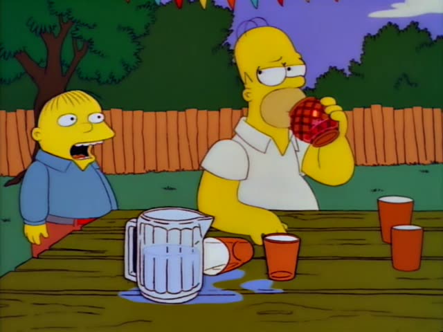 A chubby, wide-eyed boy in a blue shirt and red pants stands beside a wooden picnic table, while Homer sits at the table…