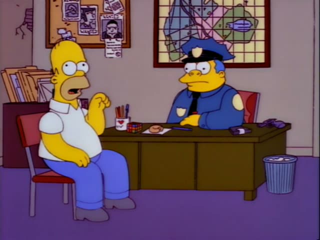 Homer Simpson sits on a red chair across a wooden desk from Chief Wiggum, the fat police chief in his blue uniform and cap…