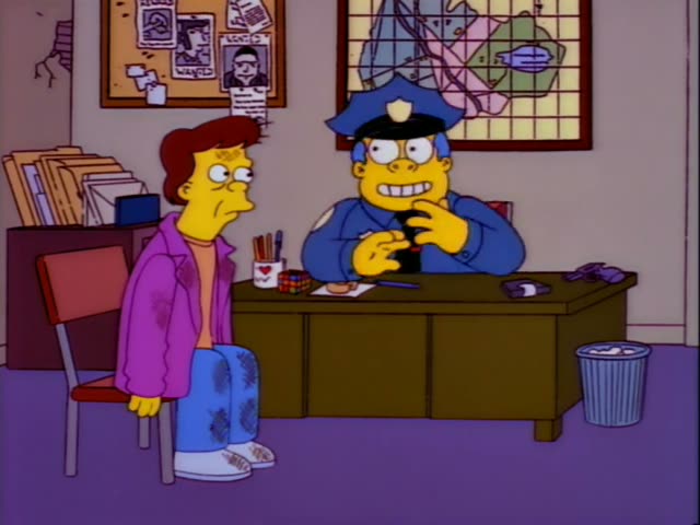 Chief Wiggum sits behind a desk in a police office while a young man with reddish-brown hair, a purple jacket and stained…
