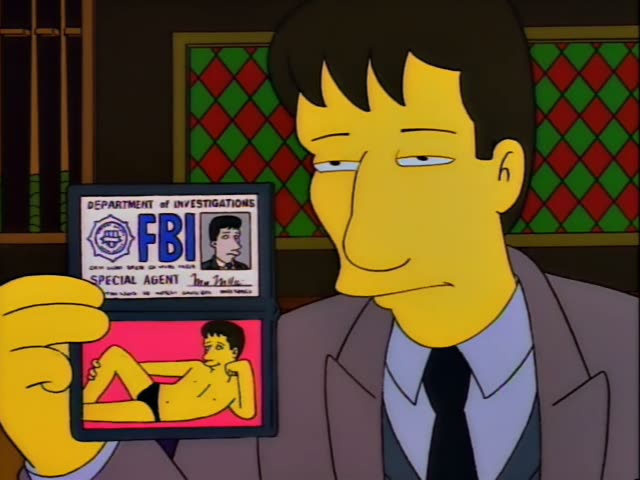 A dark-haired man in a brown suit and black tie holds up an FBI badge with a pinup photo, then talks with Moe…