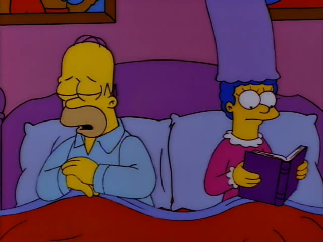 Homer Simpson and Marge Simpson lie side by side in a purple bed with a red blanket, Marge holding an open book in a pink…