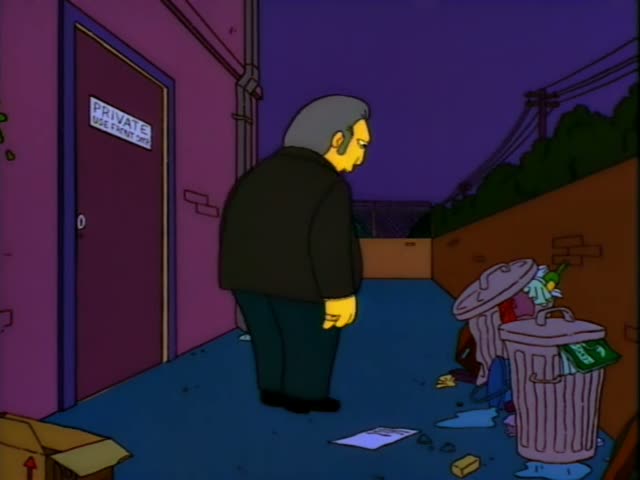 An older grey-haired man in a dark jacket and trousers stands in a blue alley beside a door with a sign reading PRIVATE USE…