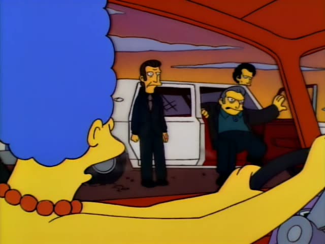 Marge Simpson sits behind the wheel of a red car while two men in dark suits stand near a white vehicle outside