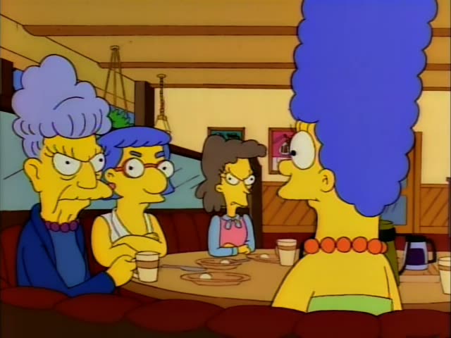 Marge Simpson sits in a diner booth across a table from her lavender-haired twin sister, Patty or Selma, while a woman…
