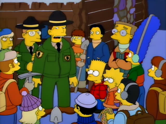 Bart and Lisa stand in the snow beside a log cabin with a search party gathered around them, including Marge with her tall…