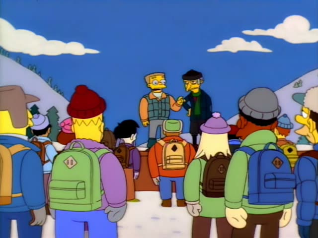 A bald man in a green vest and glasses stands on a snowy ridge beside a thin, older man with grey hair at the sides…