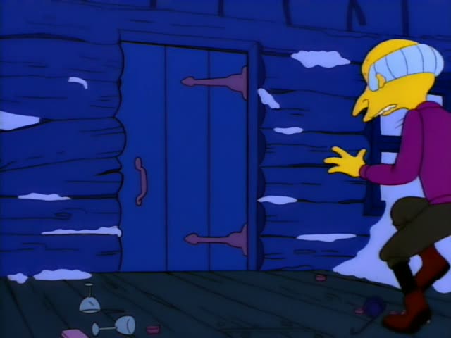 Mr. Burns wears a striped cap, a magenta sweater and olive trousers as he stands outside a blue log cabin with snow…