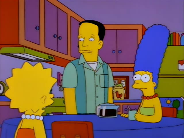 Lisa and Marge stand at a kitchen counter beside a thin, black-haired man in a green shirt and vest who gestures with one…