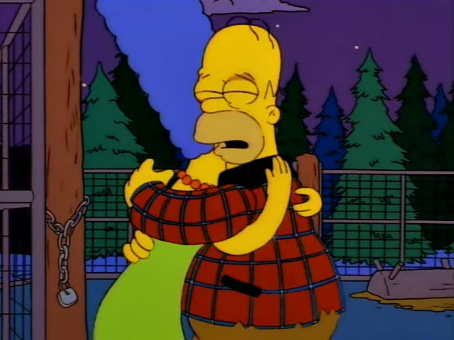 Homer and Marge stand outdoors at night beside a chain-link fence lined with pine trees, a wooden post, and a chain…