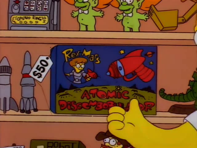 Homer stands at a toy shelf beside a thin shopkeeper with slicked black hair and a green shirt with a black collar