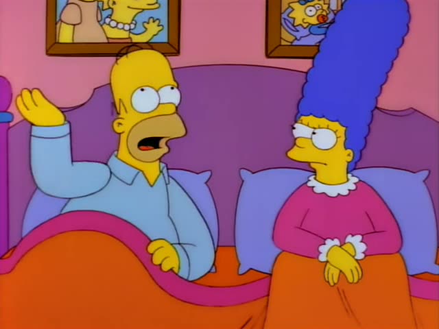 Homer Simpson and Marge Simpson sit side by side in a bed with a purple headboard and orange blanket, under framed pictures…