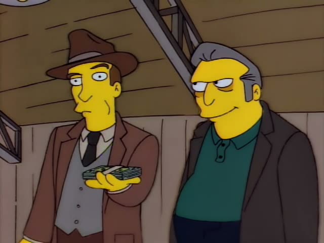 Two unnamed men in a wood-paneled room, one in a brown fedora, brown jacket, black tie and grey vest, the other with grey…